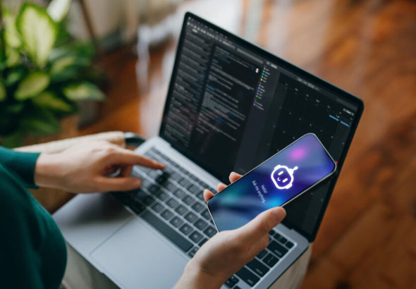 Asian woman using  AI chatbot virtual assistance app on smartphone to assist her while working on laptop. Using AI technology while working at home. Online robot system. Concept of VR and AR technologies. People, AI, innovation and technology